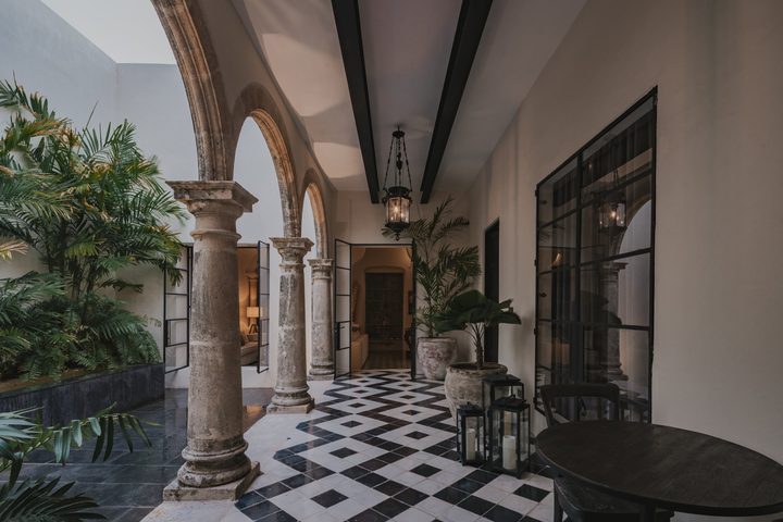 Une galerie d’arcs en pierre dans le patio de l’une des casonas de Casonas MX, avec un sol en damier, des plantes et des lanternes.