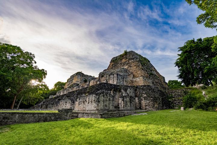 A stepped stone structure at Becán, on a grassy plaza among the trees.